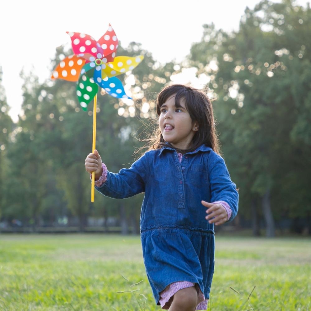 girl holding pinwheel running grass park children outdoor activity